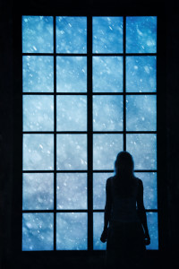 Lonely women looking at snowfall through big glass window