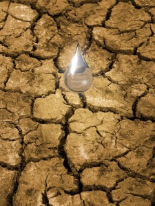Water drop falling on parched, cracked ground. Concept for importance of water resources, breaking the drought.